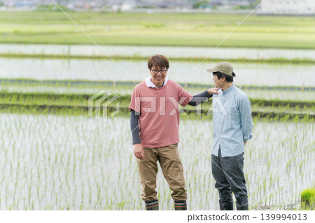 Two farmers standing on the embankment of a rice paddy. Two farmers standing on the embankment of a rice paddy. 139994013