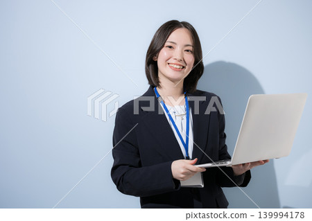 A working woman with a name tag and a laptop, against a light blue background, representing business and IT-related themes, smiling and looking directly at the camera. 139994178