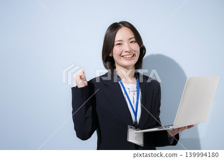 一位可愛的女員工，筆記型電腦上別著名牌，在淺藍色背景前擺出勝利的姿勢。 139994180