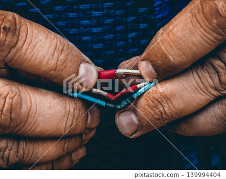 Worker performing electrical wiring, joining colorful cables using heat shrink tubing, illustrating concepts of connection, repair, craftsmanship, maintenance, and manual labor in a close-up view. Worker performing electrical wiring, joining colorful cables using heat shrink tubing, illustrating concepts of connection, repair, craftsmanship, maintenance, and manual labor in a close-up view. 139994404
