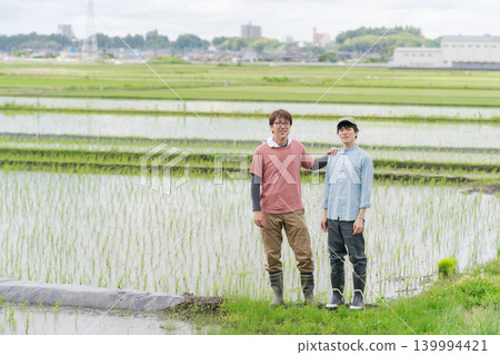 Farmers in their 20s and 50s standing on the embankment of a rice paddy. 139994421