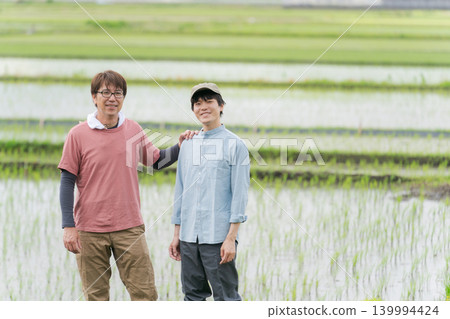 Farmers in their 20s and 50s standing on the embankment of a rice paddy. Farmers in their 20s and 50s standing on the embankment of a rice paddy. 139994424