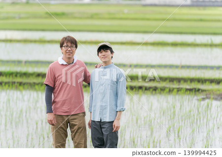 20多歲和50多歲的農民站在稻田堤岸上。 20多歲和50多歲的農民站在稻田堤岸上。 139994425