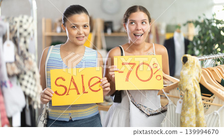 Two young women holding discount signs in clothing store Two young women holding discount signs in clothing store 139994670