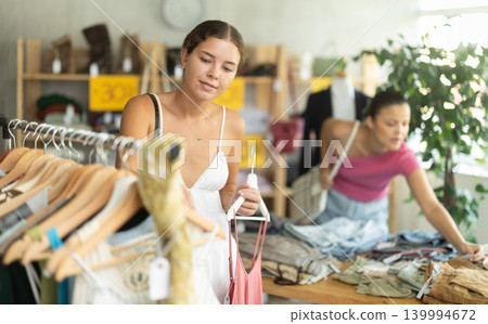 Positive joyful woman looking for fashionable clothes in clothing boutique Positive joyful woman looking for fashionable clothes in clothing boutique 139994672