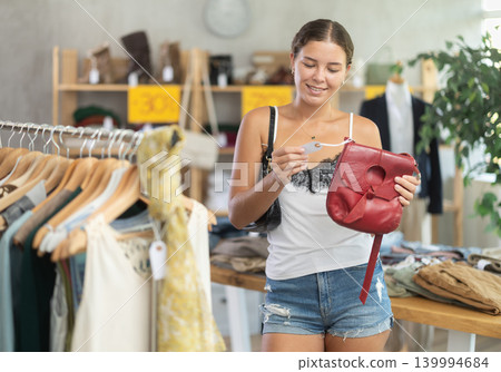 Happy young woman choosing handbag in clothing store Happy young woman choosing handbag in clothing store 139994684