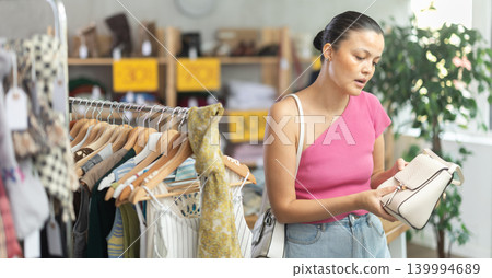 Selective young Asian woman choosing handbag in clothing store Selective young Asian woman choosing handbag in clothing store 139994689
