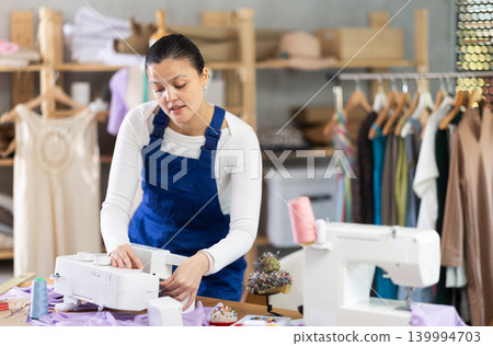 Skilled young repairwoman repairing sewing-machine Skilled young repairwoman repairing sewing-machine 139994703
