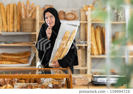 Young woman in Muslim clothing choosing pastries in bakery 139994728