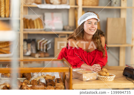 Smiling happy girl in red dress behind bakery counter Smiling happy girl in red dress behind bakery counter 139994735