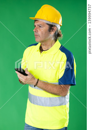 Employee in a protective helmet with a mobile phone against the background of chromakey. Employee in a protective helmet with a mobile phone against the background of chromakey. 139994737