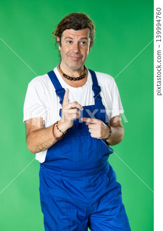 Handyman in overalls standing on a green background Handyman in overalls standing on a green background 139994760