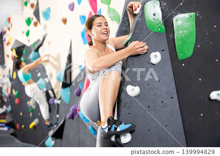 Young female alpinist practicing indoor a rock-climbing on a artificial boulder without safety belts 139994829