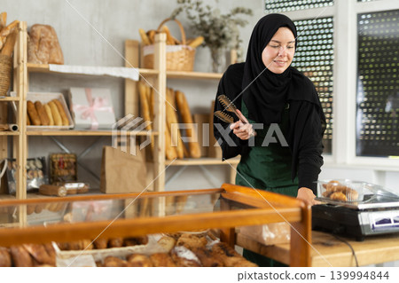Girl seller of an oriental bakery in traditional muslim clothes with fresh hot croissants in hands Girl seller of an oriental bakery in traditional muslim clothes with fresh hot croissants in hands 139994844