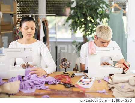 Two seamstresses male and female working on sewing machines in sewing workshop Two seamstresses male and female working on sewing machines in sewing workshop 139994850