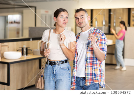 Friendly young couple looking for bathroom fixtures in showroom Friendly young couple looking for bathroom fixtures in showroom 139994872