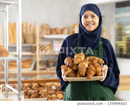 Asian Muslim woman bakery worker sells croissants, stand at counter and wait for visitors Asian Muslim woman bakery worker sells croissants, stand at counter and wait for visitors 139994883