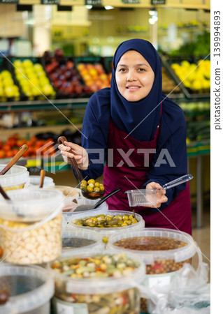 Young woman in hijab selling olives in supermarket Young woman in hijab selling olives in supermarket 139994893