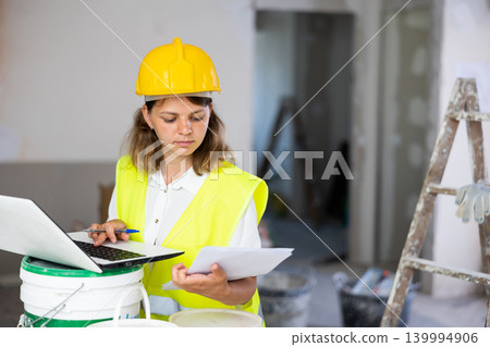Woman builder checking documentation, using laptop Woman builder checking documentation, using laptop 139994906