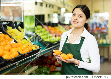 Young woman in uniform sells tangerines in grocery store 139994917
