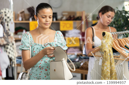 Selective young Asian woman choosing handbag in clothing store Selective young Asian woman choosing handbag in clothing store 139994937