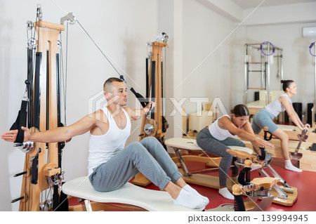 Sportive young guy training her arms pulling handle of cable exercise machine Sportive young guy training her arms pulling handle of cable exercise machine 139994945