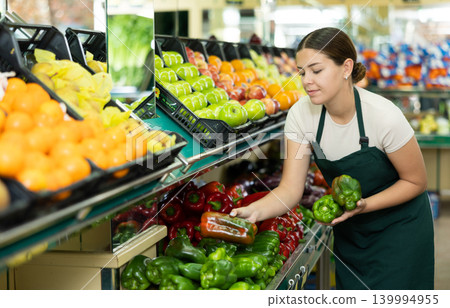 Female seller in apron chooses juicy bell pepper 139994955
