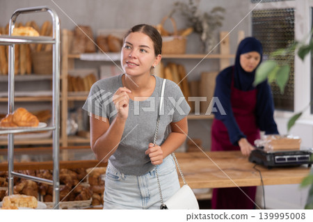 Young girl chooses some bakery goods while Muslim seller works in background in baker's Young girl chooses some bakery goods while Muslim seller works in background in baker's 139995008