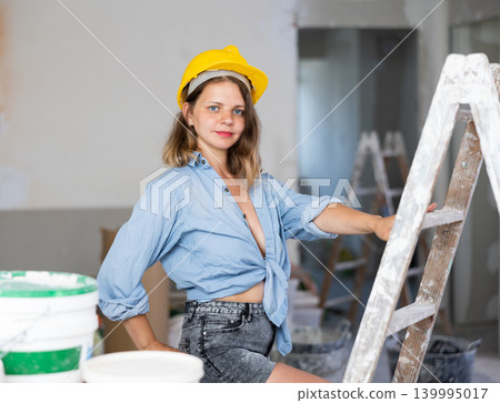 Seductive woman in hardhat and denim shirt posing next to a stepladder in room being renovated Seductive woman in hardhat and denim shirt posing next to a stepladder in room being renovated 139995017