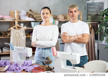 Young male and female dressmakers posing in sewing workshop Young male and female dressmakers posing in sewing workshop 139995040