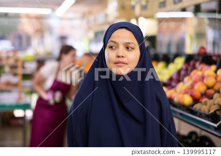 Portrait of young woman in veil, walking with a shopper cart, making necessary purchases Portrait of young woman in veil, walking with a shopper cart, making necessary purchases 139995117