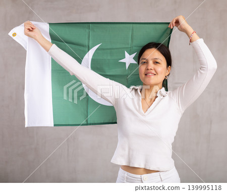 Reliant positive young woman holds big national flag of Pakistan with confident smile showing teeth Reliant positive young woman holds big national flag of Pakistan with confident smile showing teeth 139995118