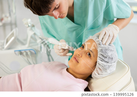Young male cosmetologist doing cleansing procedure to young woman Young male cosmetologist doing cleansing procedure to young woman 139995126