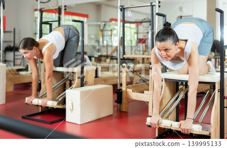 Young girl doing exercises standing on knees on combo chair Young girl doing exercises standing on knees on combo chair 139995133