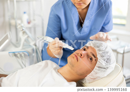 Young woman cosmetologist doing exfoliation to young man Young woman cosmetologist doing exfoliation to young man 139995168