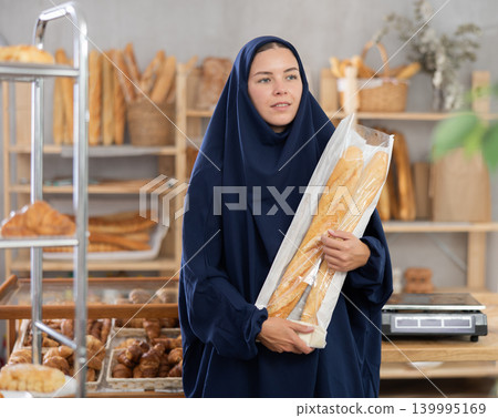 Portrait of an oriental girl in abaya with fresh baguettes in her hands in bakery Portrait of an oriental girl in abaya with fresh baguettes in her hands in bakery 139995169