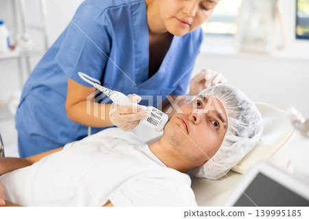 Young woman cosmetologist doing whitening procedure to young man Young woman cosmetologist doing whitening procedure to young man 139995185