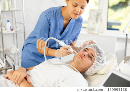 Young woman cosmetologist doing cleansing procedure to young man 139995188