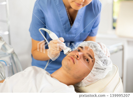 Young woman cosmetologist doing ultrasound procedure to young man Young woman cosmetologist doing ultrasound procedure to young man 139995207