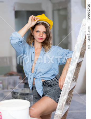 Sexy woman in denim shirt and shorts next to a stepladder in room being renovated 139995230