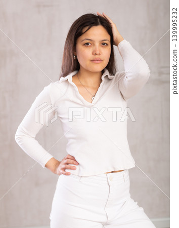 Studio portrait of pretty young Asian girl in a white trouser suit on gray background Studio portrait of pretty young Asian girl in a white trouser suit on gray background 139995232