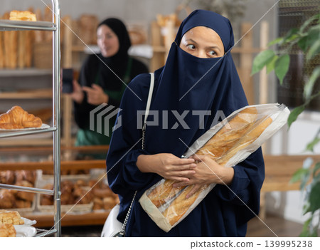 Muslim woman in niqab with baguettes in hands shopping at bakery 139995238