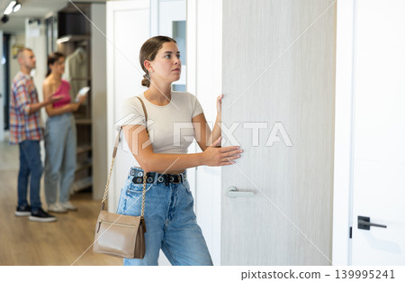 Young female buyer carefully selects an interior door in hardware store Young female buyer carefully selects an interior door in hardware store 139995241