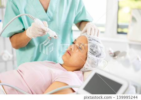 Young male cosmetologist doing moisturizing procedure to young woman Young male cosmetologist doing moisturizing procedure to young woman 139995244