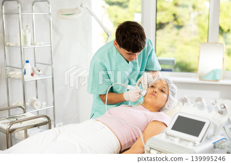 Young male cosmetologist doing ultrasound procedure to young woman Young male cosmetologist doing ultrasound procedure to young woman 139995246