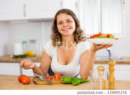 Portrait of woman cooking and eating salad at home 139995258
