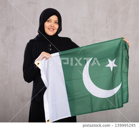 Young Muslim woman in black hijab holds unfurled flag of Pakistan. Young Muslim woman in black hijab holds unfurled flag of Pakistan. 139995295