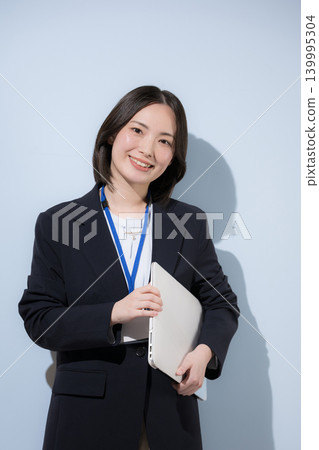 一位可愛的女員工,戴著名牌,手持筆記型電腦,站在淺藍色背景前,直視鏡頭,展現出專業的商務和IT形象。 一位可愛的女員工,戴著名牌,手持筆記型電腦,站在淺藍色背景前,直視鏡頭,展現出專業的商務和IT形象。 139995304