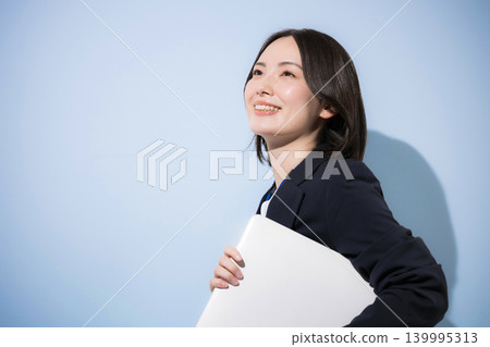 一位可愛的女員工,戴著名牌,手持筆記型電腦,抬頭看著淺藍色背景,代表商業和IT相關主題。 一位可愛的女員工,戴著名牌,手持筆記型電腦,抬頭看著淺藍色背景,代表商業和IT相關主題。 139995313