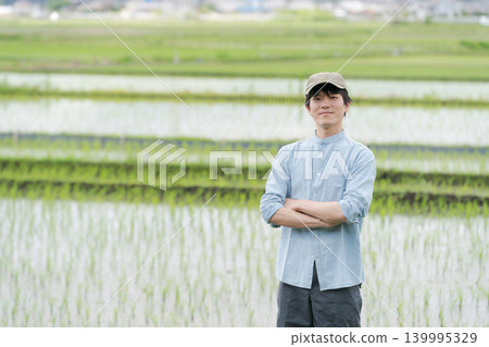 A young farmer stands on the path between rice paddies. A young farmer stands on the path between rice paddies. 139995329
